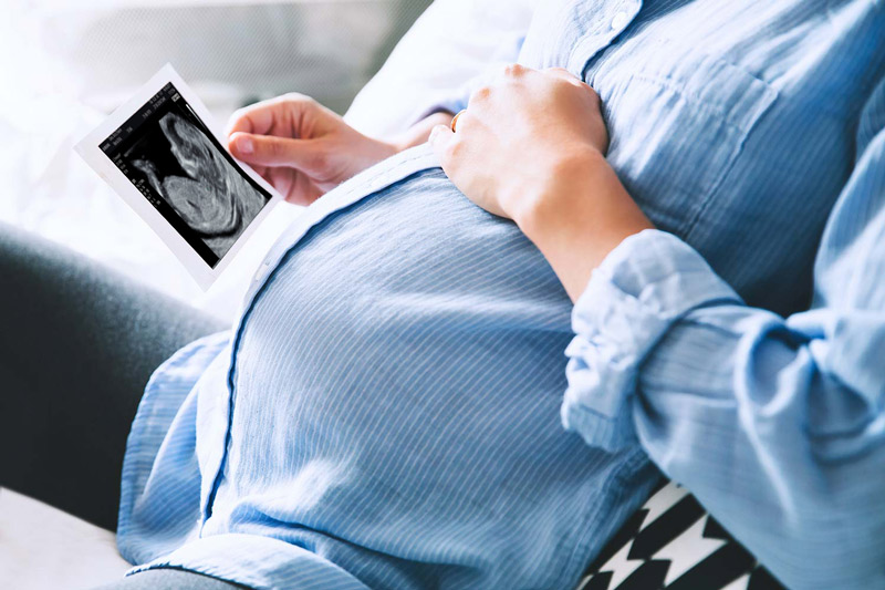 Schwangere Frau hält das Ultraschallbild in den Händen